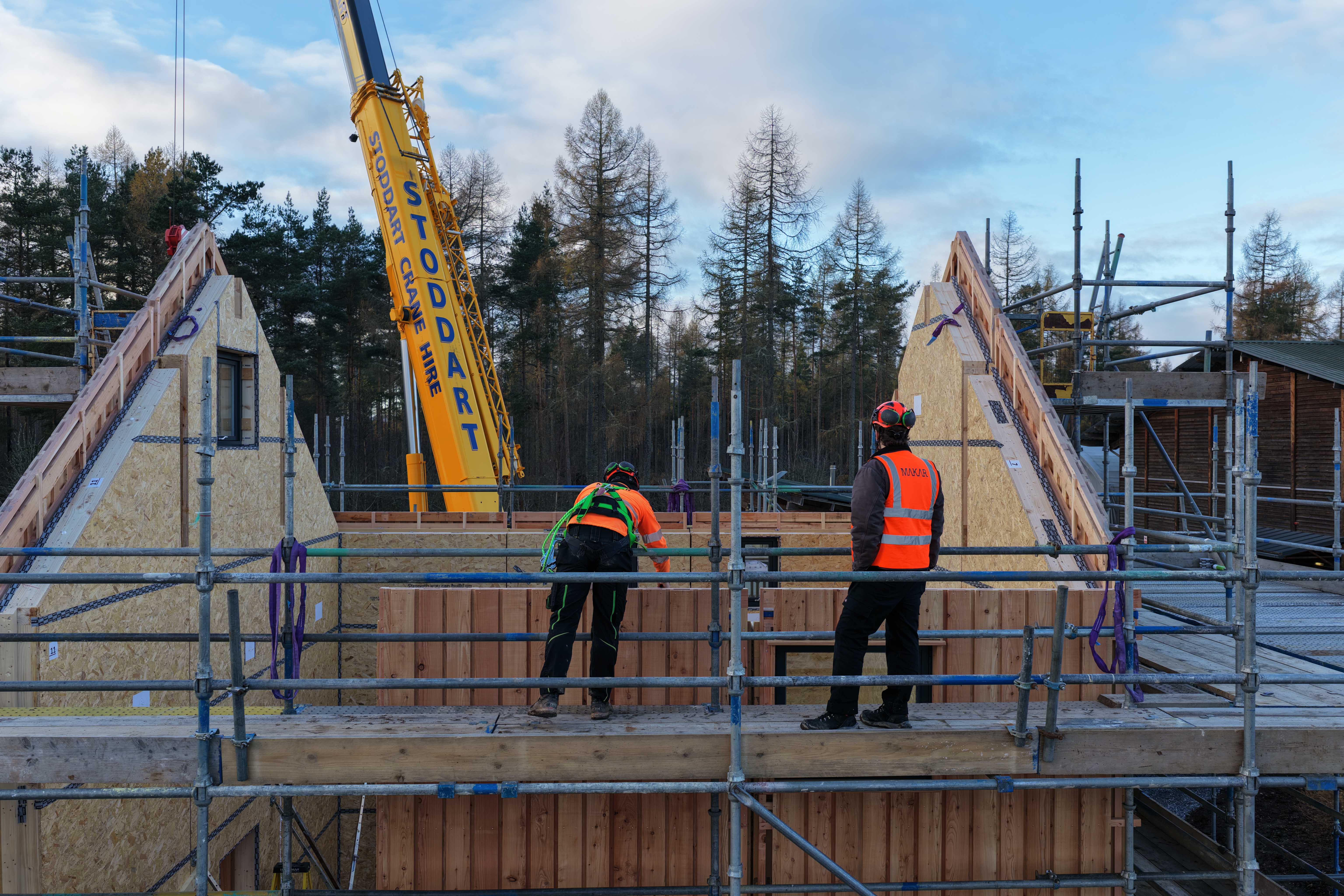 Two workets in PPE stand on a scaffolded platform to see the prototype home during assembly.