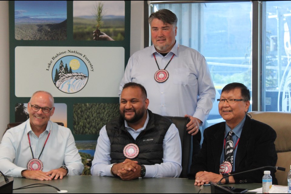Four men wearing conference badges sit and stand around a table at a meeting, with a Lake Babine Nation Forestry banner displayed in the background.