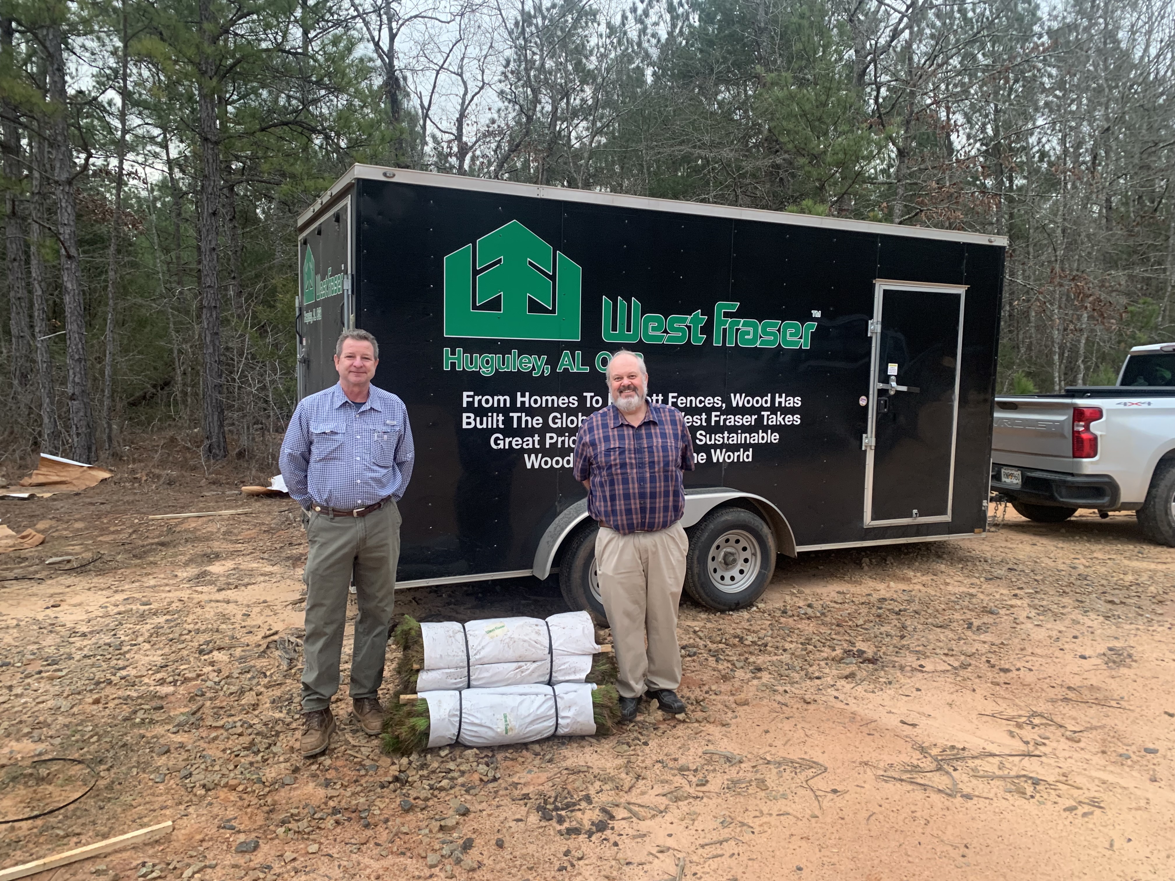 Two men stand in front of a black trailer labeled