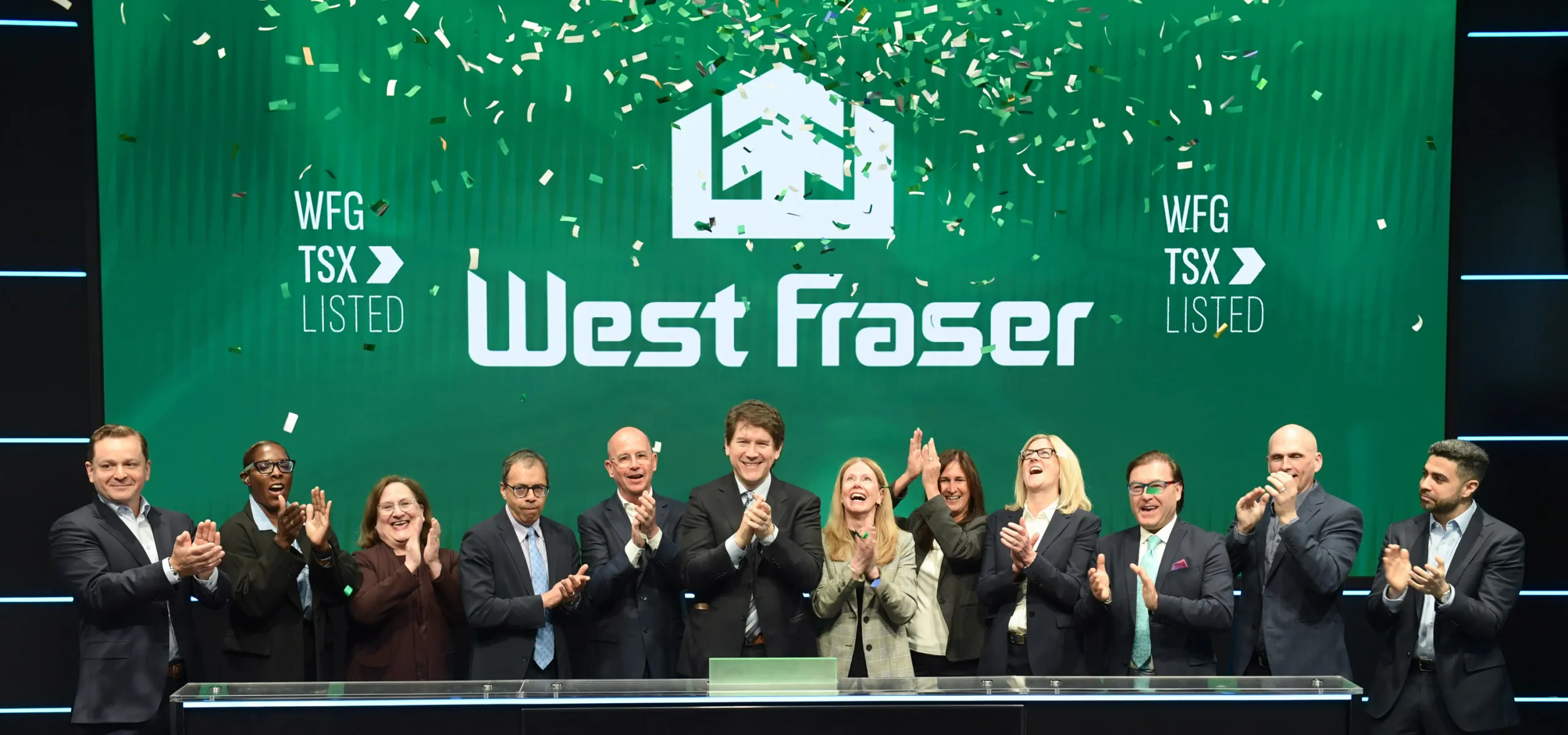 A group of West Fraser team member celebrate at the bell ringing as confetti falls on stage at the Toronto Stock Exchange, with a sign reading “West Fraser” and “The Market is Open.”