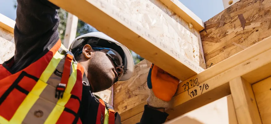 Construction worker in safety gear inspecting wooden framing on a building site.