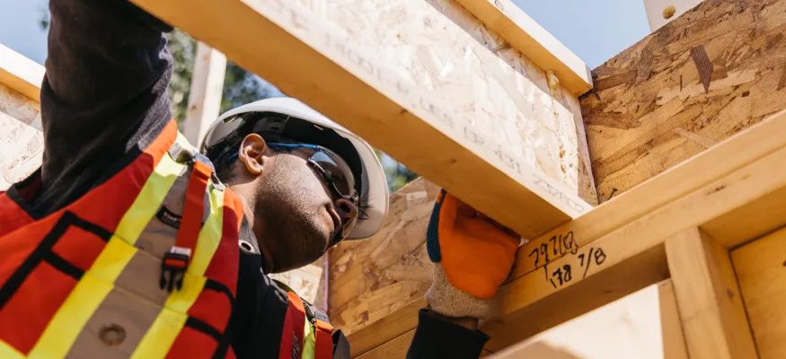 Construction worker in safety gear inspecting wooden framing on a building site.