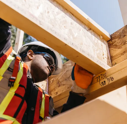 Construction worker in safety gear inspecting wooden framing on a building site.