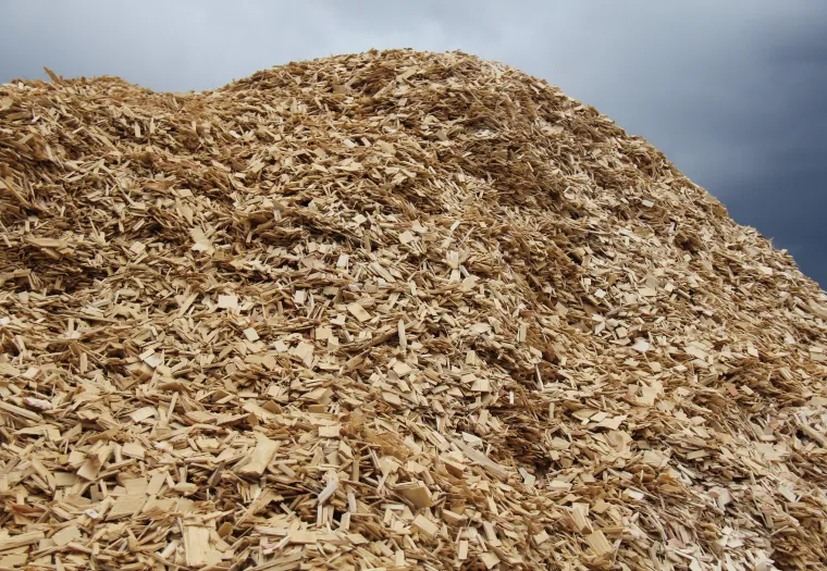 A large pile of wood chips with a cloudy sky in the background.