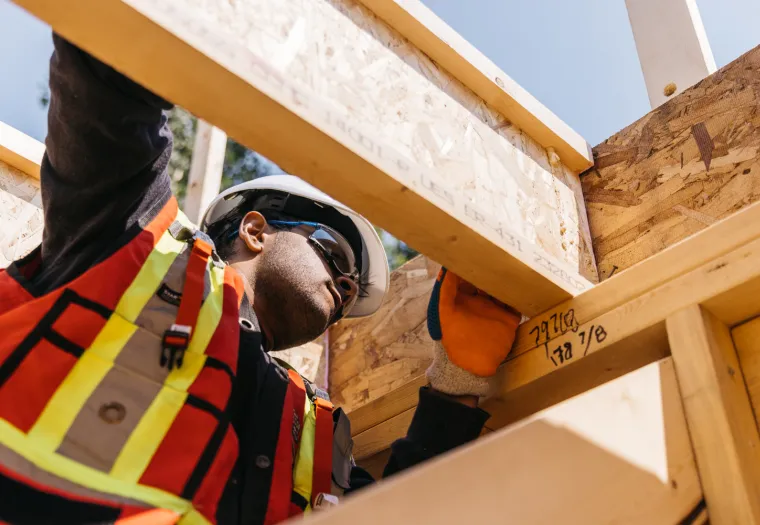 Construction worker in safety gear inspecting wooden framing on a building site.