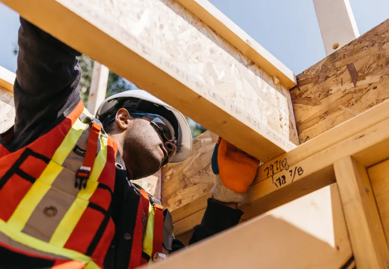 Construction worker in safety gear inspecting wooden framing on a building site.