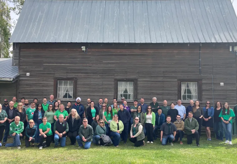 West Fraser team members pose in front of a wooden barn structure, on the site of the company's Quesnel location.