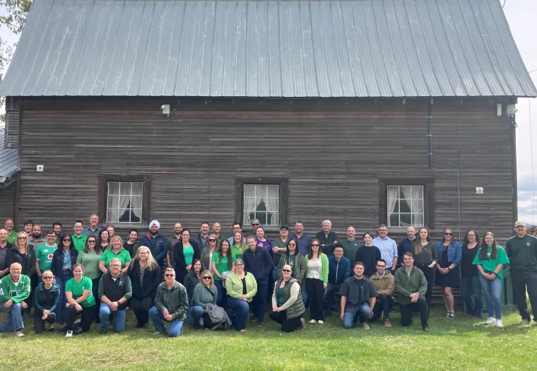 West Fraser team members pose in front of a wooden barn structure, on the site of the company's Quesnel location.