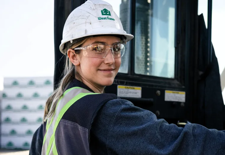 A person wearing a hard hat, safety glasses, and reflective vest stands beside industrial equipment, looking at the camera.