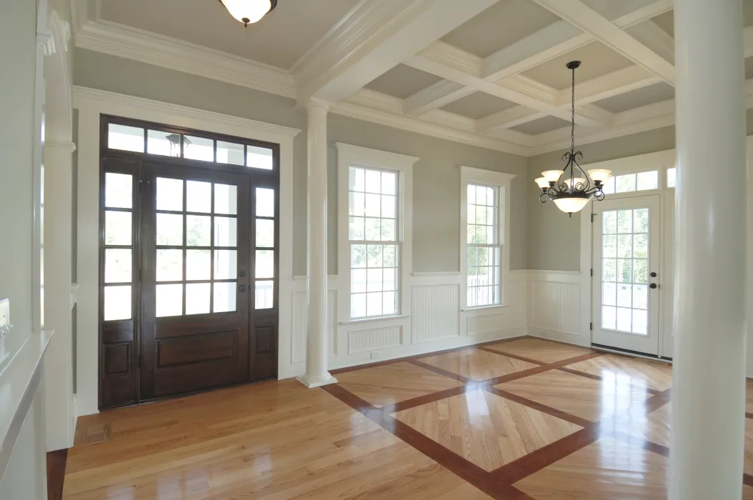 Bright entryway and dining area with wood floors, large windows, glass doors, coffered ceiling, and white trim.