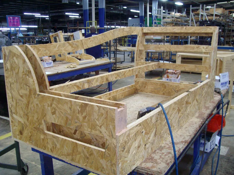 A partially assembled wooden couch frame made of oriented strand board sits on a workbench in a furniture manufacturing factory.