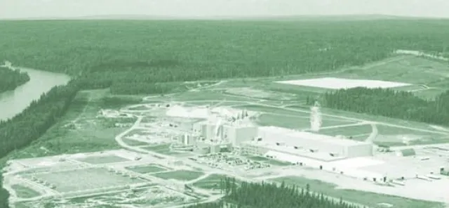Aerial view of an industrial facility surrounded by forested land, with a river on the left side of the image.