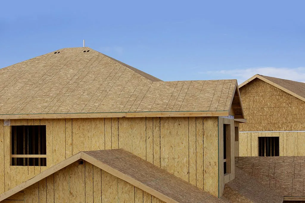 Newly constructed homes with exposed wood sheathing on roofs and walls under a clear blue sky.