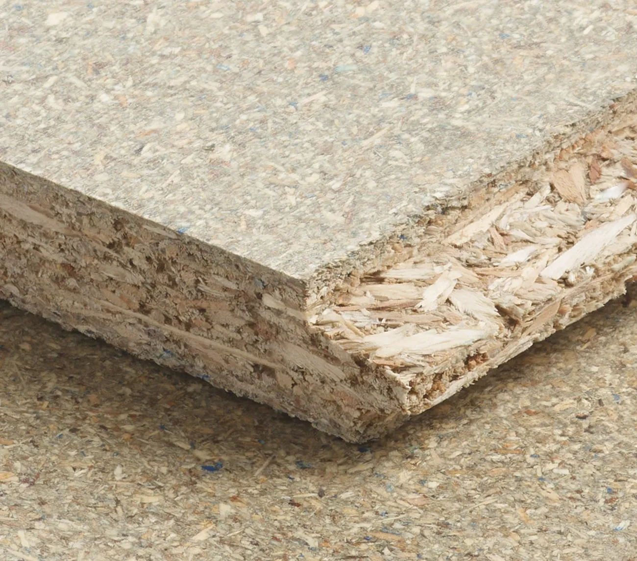 Close-up of a textured particle board showing layers of compressed wood chips and fibers on a flat surface.