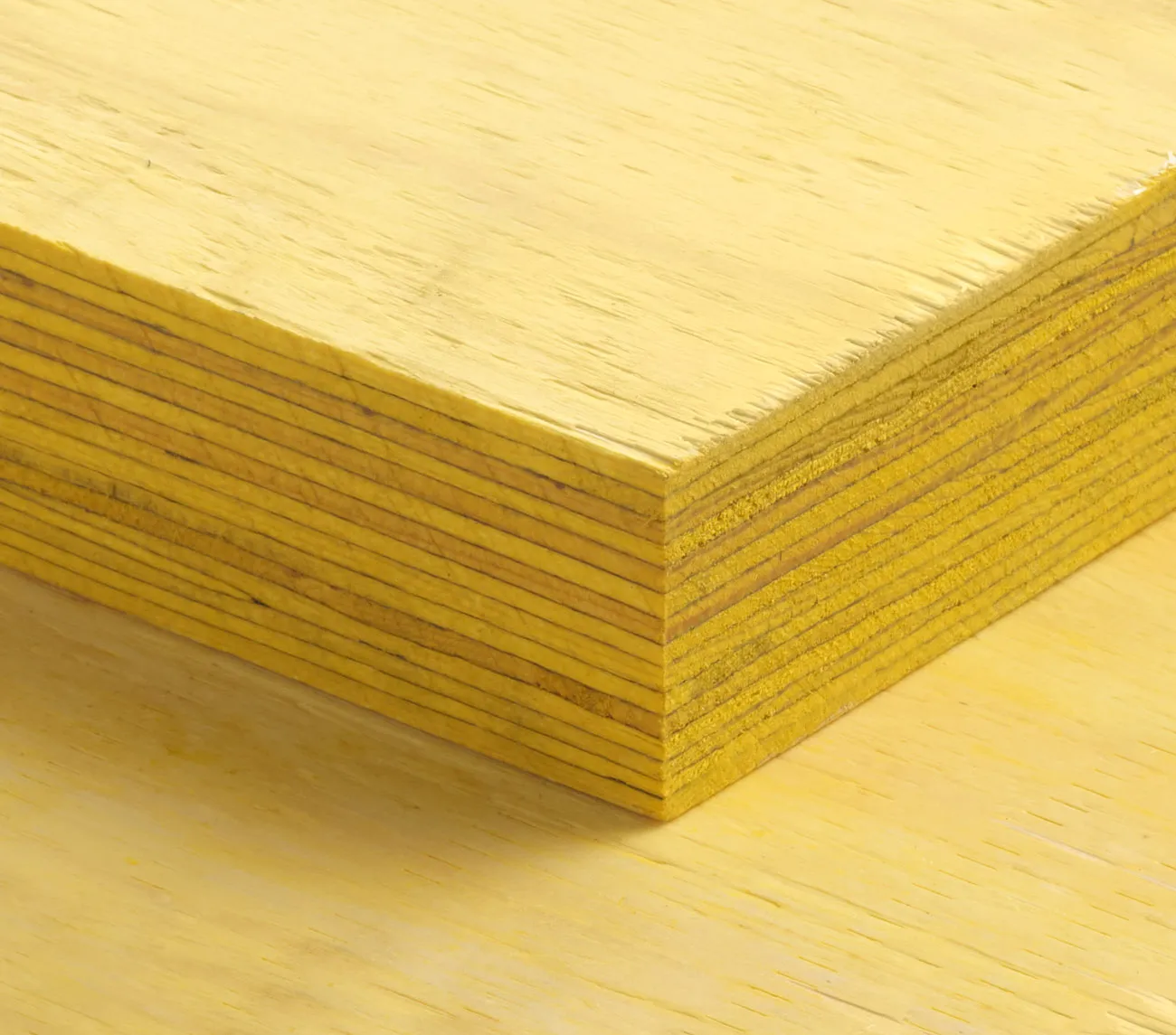 Close-up of a stack of yellow plywood sheets with visible layers and a smooth surface.