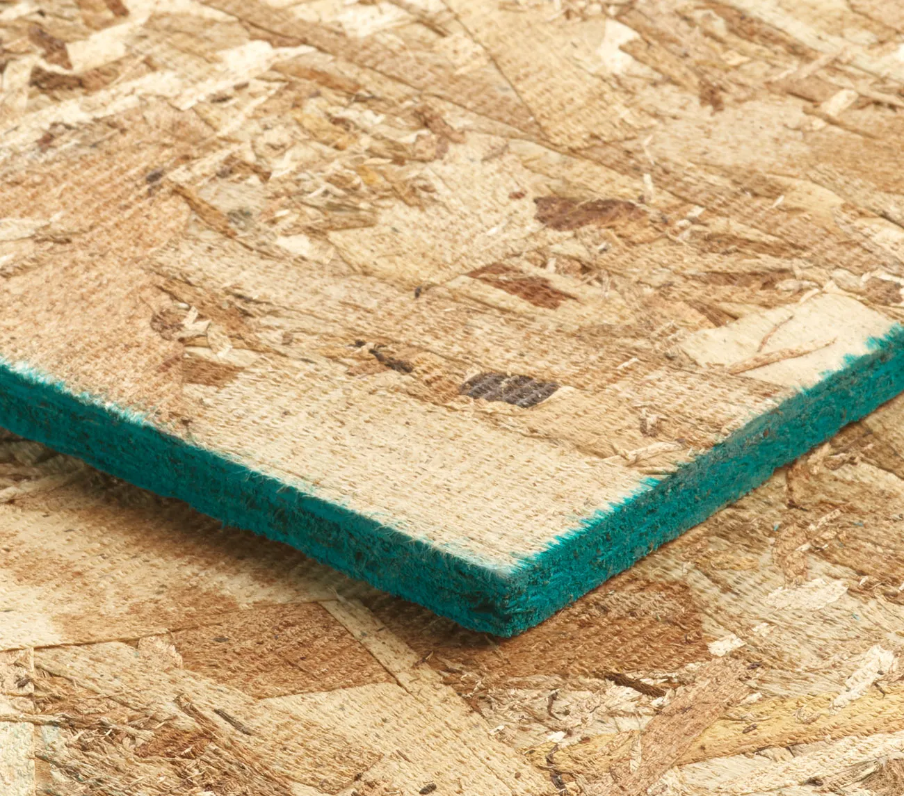 Close-up of a wooden chipboard panel with a green edge, resting on another identical panel.