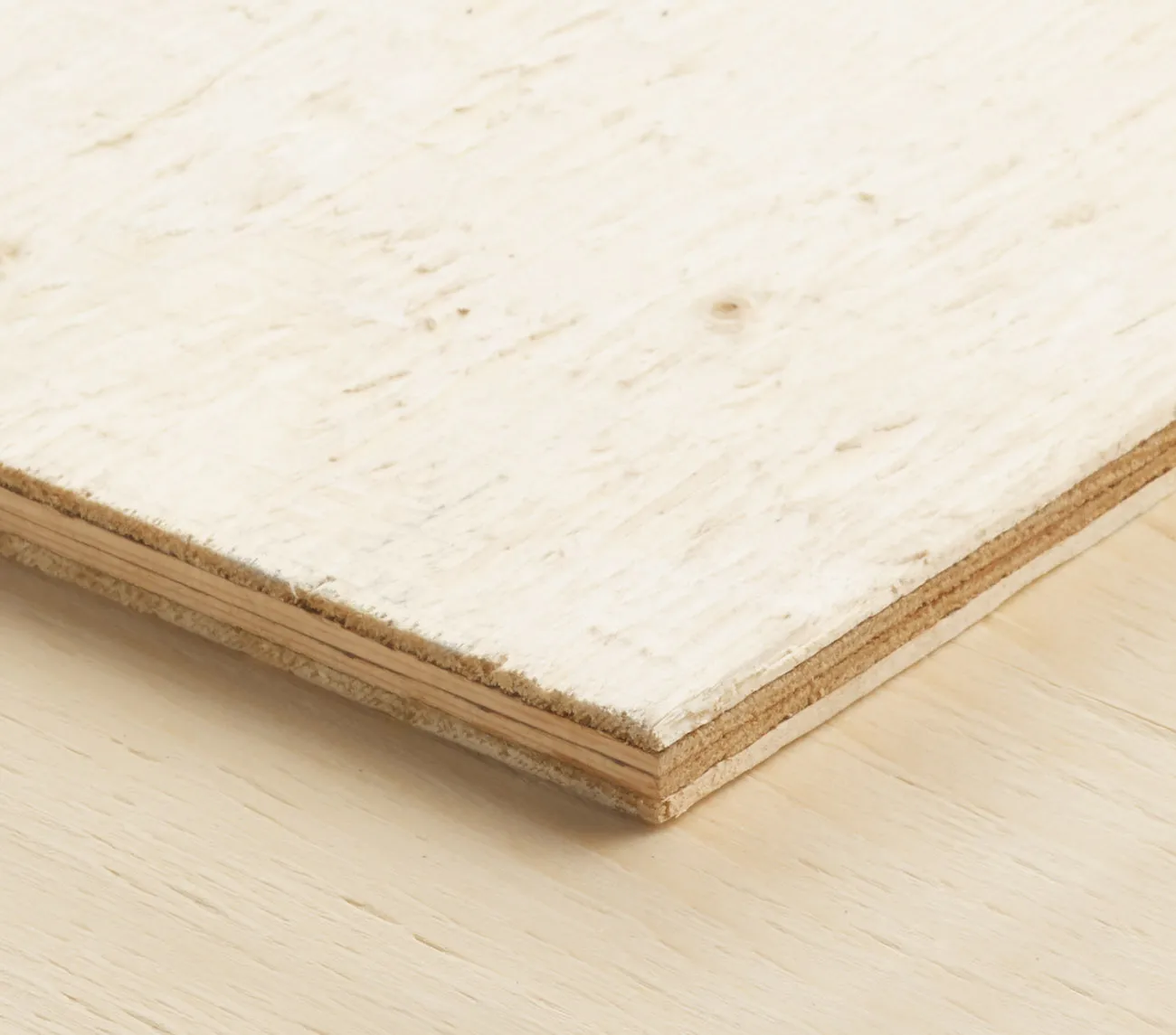 A close-up of the corner of a wood panel showing its layered structure, placed on a light wooden surface.