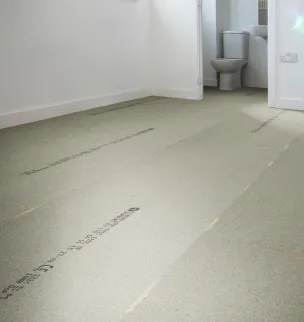 Empty room with a light gray underlayment floor, white walls, and a view into a bathroom with a toilet.