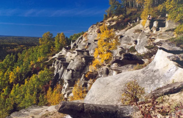 Rocky hillside with scattered yellow and green trees under a clear blue sky, showing a mix of stone formations and forested landscape.