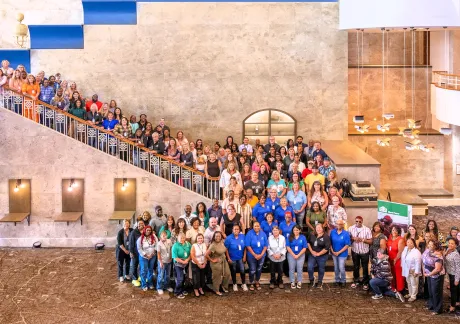 A large group of people posed for a photo on a staircase and in the lobby of a modern building. Various individuals are dressed in casual clothing indicating a diverse group assembly.