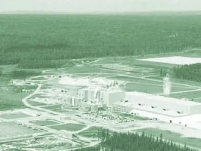 Aerial view of an industrial facility surrounded by forested land, with a river on the left side of the image.