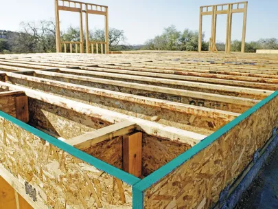 Construction site featuring a wooden framework for a building's floor with wall frames positioned in the background under a clear sky.