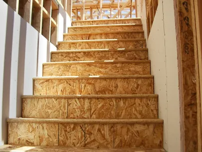 Wooden stairs in a partially constructed building, surrounded by exposed framing and drywall.