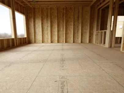 An unfinished room with framed walls and large windows, showing bare wooden flooring and insulation.