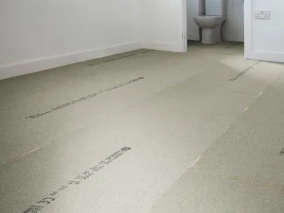 Empty room with a light gray underlayment floor, white walls, and a view into a bathroom with a toilet.