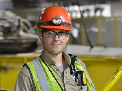 A person wearing a hard hat, safety glasses, and a reflective vest stands in an industrial environment.