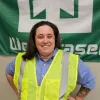 A person wearing a yellow safety vest stands smiling in front of a green and white banner.