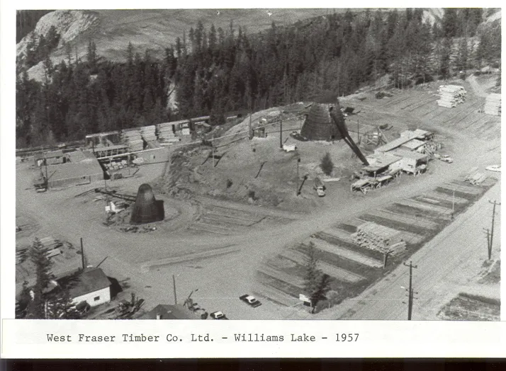 Aerial view of West Fraser Timber Co. Ltd. site in Williams Lake, 1957, showing lumber stacks, industrial structures, and surrounding trees, with vehicles and buildings visible.